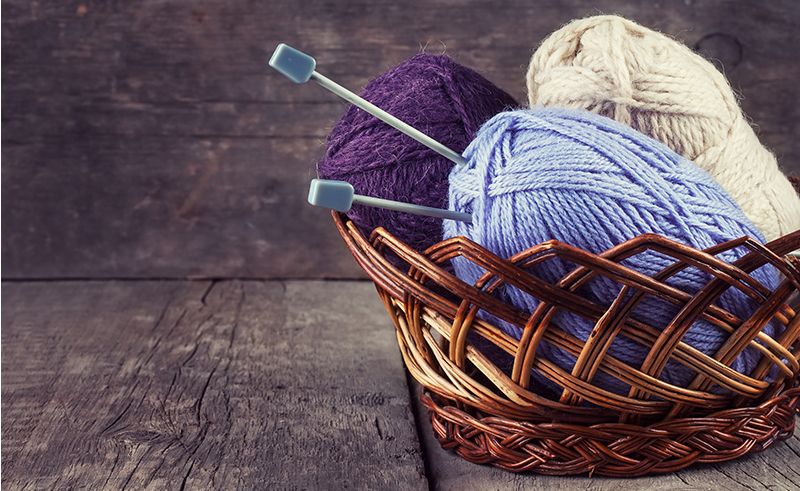 Skeins colored yarn and knitting needles in a basket on a wooden background