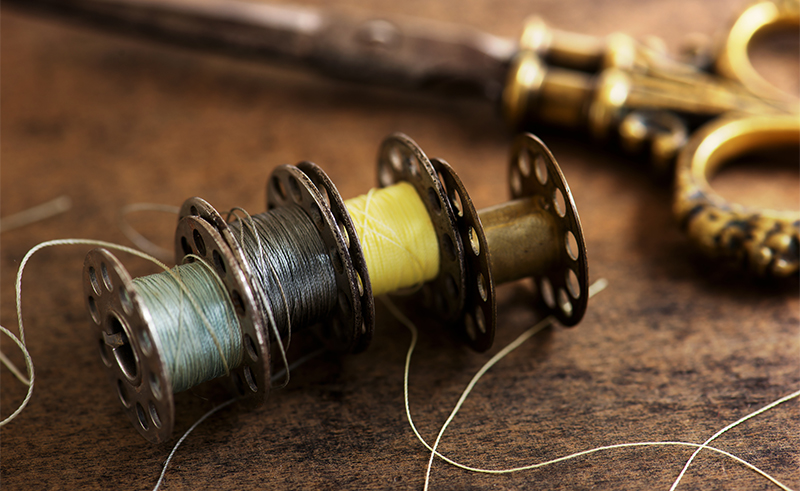 Vintage sewing machine bobbins with vintage gold ( brass ) scissors on a old grungy work table. Tailor's work table. textile or fine cloth making. Shallow depth of field.