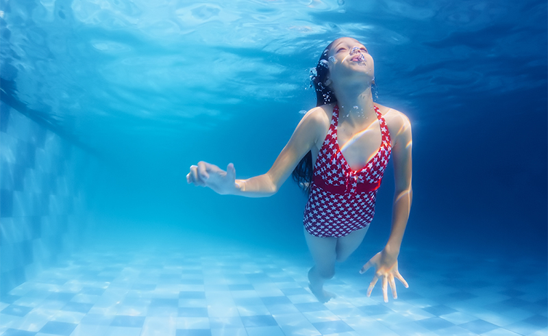 Child swimming underwater lesson - girl diving with fun in blue pool. Healthy active family lifestyle physical development and children water sports activity with parents on summer vacation with kids